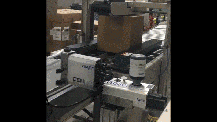 A FoxJet printer in action printing on a cardboard box.