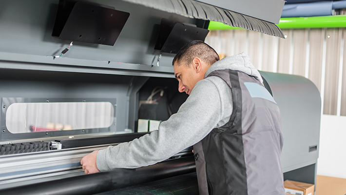 A technician performs maintenance on an industrial printer in a factory.