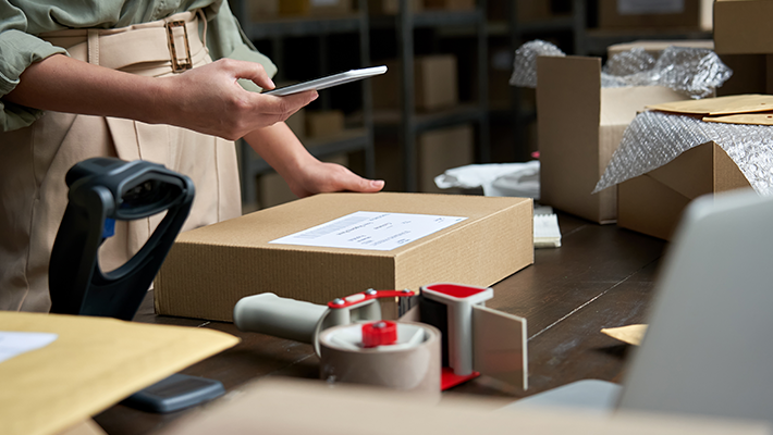 A woman prepares parcels for shipment with self-adhesive labels and a barcode reader.